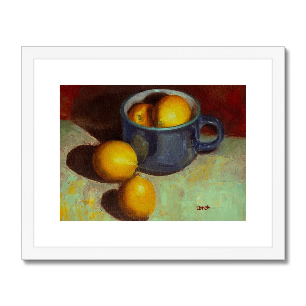 Painting of lemons sitting in and beside a blue teacup. Framed with a white frame and white mount. 